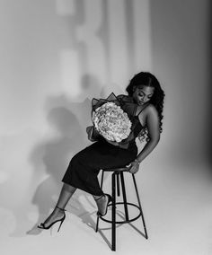 a black and white photo of a woman sitting on a stool with flowers in her hands