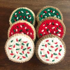 four crocheted coasters with red, green and white designs sitting on top of a wooden table