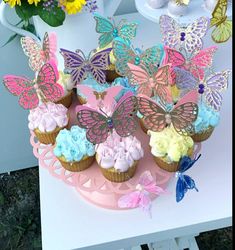 cupcakes decorated with butterflies and flowers on a pink cake stand in front of yellow daisies