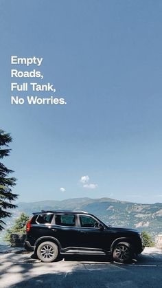 a black suv parked on the side of a road with an empty road and mountains in the background