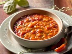 a white bowl filled with chili sauce on top of a plate next to a spoon