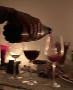 a person pouring wine into glasses on a counter with candles and other items in the background