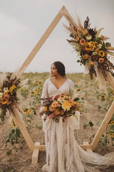 a woman standing in front of a wooden frame with flowers on it and holding a bouquet