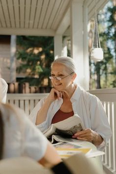 an older woman sitting on a porch talking to another woman who is holding a magazine