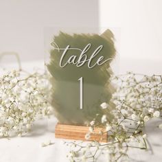 the table number is placed on top of a wooden stand with baby's breath flowers