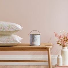 two white vases with pink flowers on a wooden bench next to a painted wall