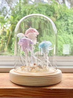 two small figurines under a glass dome on a wooden stand in front of a window