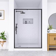 a white bathroom with a black frame and glass shower stall door, wood side table and mirror on the wall