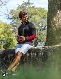 a man sitting on top of a stone wall next to a tree