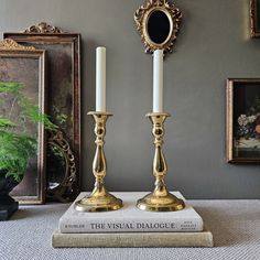 two gold candlesticks sitting on top of a book in front of a mirror