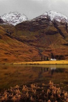 the mountains are covered in snow and brown grass, with a small lake below them