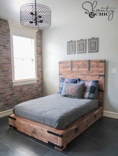 a bed made out of pallet wood in a room with brick walls and windows