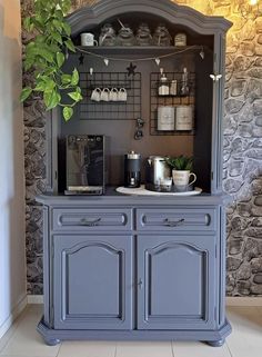 an old fashioned china cabinet painted in blue and grey with shelves on each side that hold cups, tea kettles and mugs