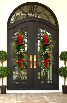 two christmas wreaths on the front door of a house with potted plants and flowers