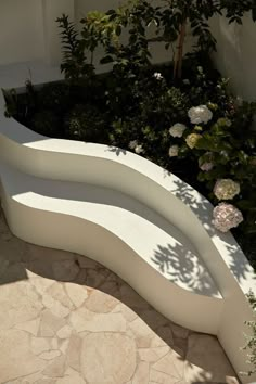 a white bench sitting in the middle of a garden next to some bushes and flowers