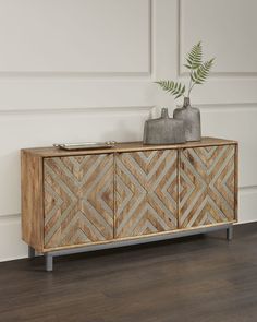 a wooden sideboard with two vases on top of it and a plant in the corner