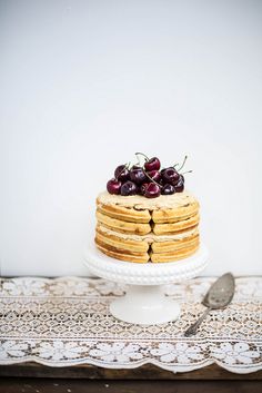 a stack of pancakes topped with cherries on top of a white cake platter