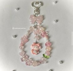 a key chain with charms and beads on top of a white surface, featuring a pink teddy bear