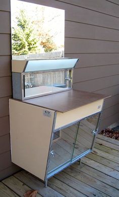 an outdoor kitchen on a deck with a small window in the back ground and wood flooring