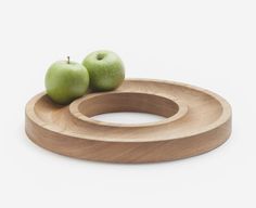 two green apples sitting on top of a wooden ring shaped tray with an apple in the middle