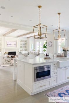 a large kitchen with white cabinets and an island that has gold lights hanging from it