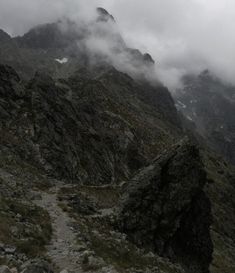 a mountain with some very tall mountains in the background and clouds coming out of it