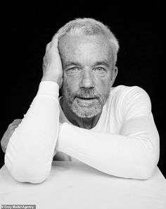 black and white photograph of an older man sitting at a table with his hands on his head