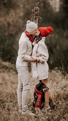 a couple kissing in the middle of a field with a dog wearing a scarf around their neck