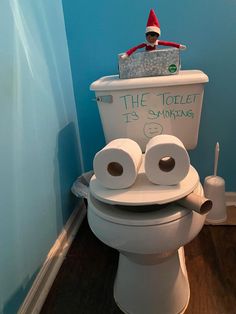 an elf is sitting on top of a toilet with two rolls of toilet paper in front of it