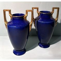 two blue vases sitting next to each other on a white counter top with gold handles