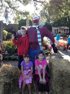 three children sitting on hay bales in front of a scarecrow and an old man