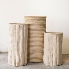 three white vases sitting next to each other on top of a cement flooring