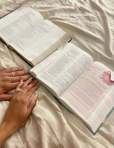 a person laying on a bed with an open book in front of them and their hands resting on the pages