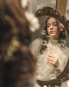 a woman is looking at herself in the mirror with flowers on her head and she is wearing a white dress