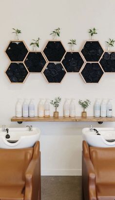 two brown leather chairs sitting in front of a wall mounted shelf with bottles and soaps on it