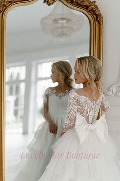 two women in wedding gowns looking at themselves in a mirror with the reflection of them