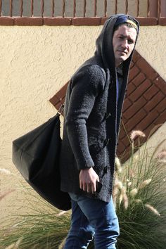 a man walking down the street with a bag in his hand and wearing a hoodie