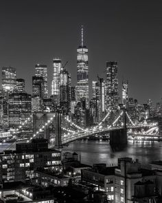 black and white photograph of the brooklyn bridge at night with city lights in the background