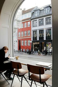 a person sitting at a table in front of an open window looking out onto the street