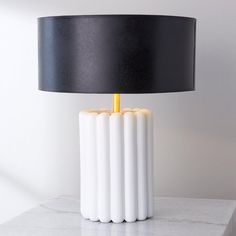 a white table lamp sitting on top of a marble counter next to a black lampshade