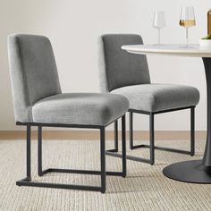 two gray chairs sitting next to each other on top of a rug near a table