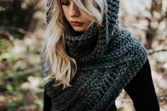 a woman with blonde hair wearing a gray knitted cowl scarf and hood in the woods