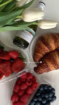 some strawberries blueberries and croissants on a white table with tulips