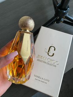 a hand holding a bottle of perfume next to a box