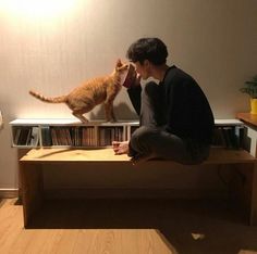 a man sitting on top of a wooden table next to a cat standing on it