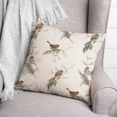 a throw pillow with birds on it sitting on a chair in front of a blanket