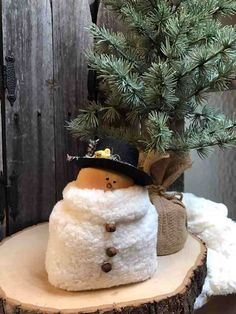 a snowman sitting on top of a tree stump next to a small pine tree