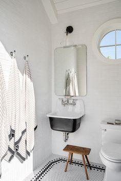 a white bathroom with black and white checkered flooring, round window, and mirror