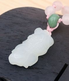 a white jade beaded necklace with pink and green beads sitting on top of a wooden table