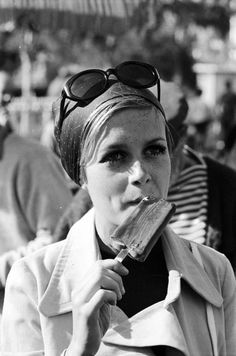 a black and white photo of a woman eating an ice cream cone in front of a crowd